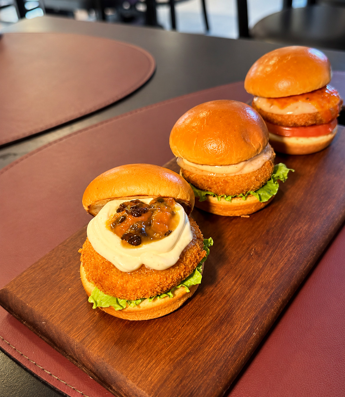 Três mini burgers artesanais servidos em uma tábua de madeira